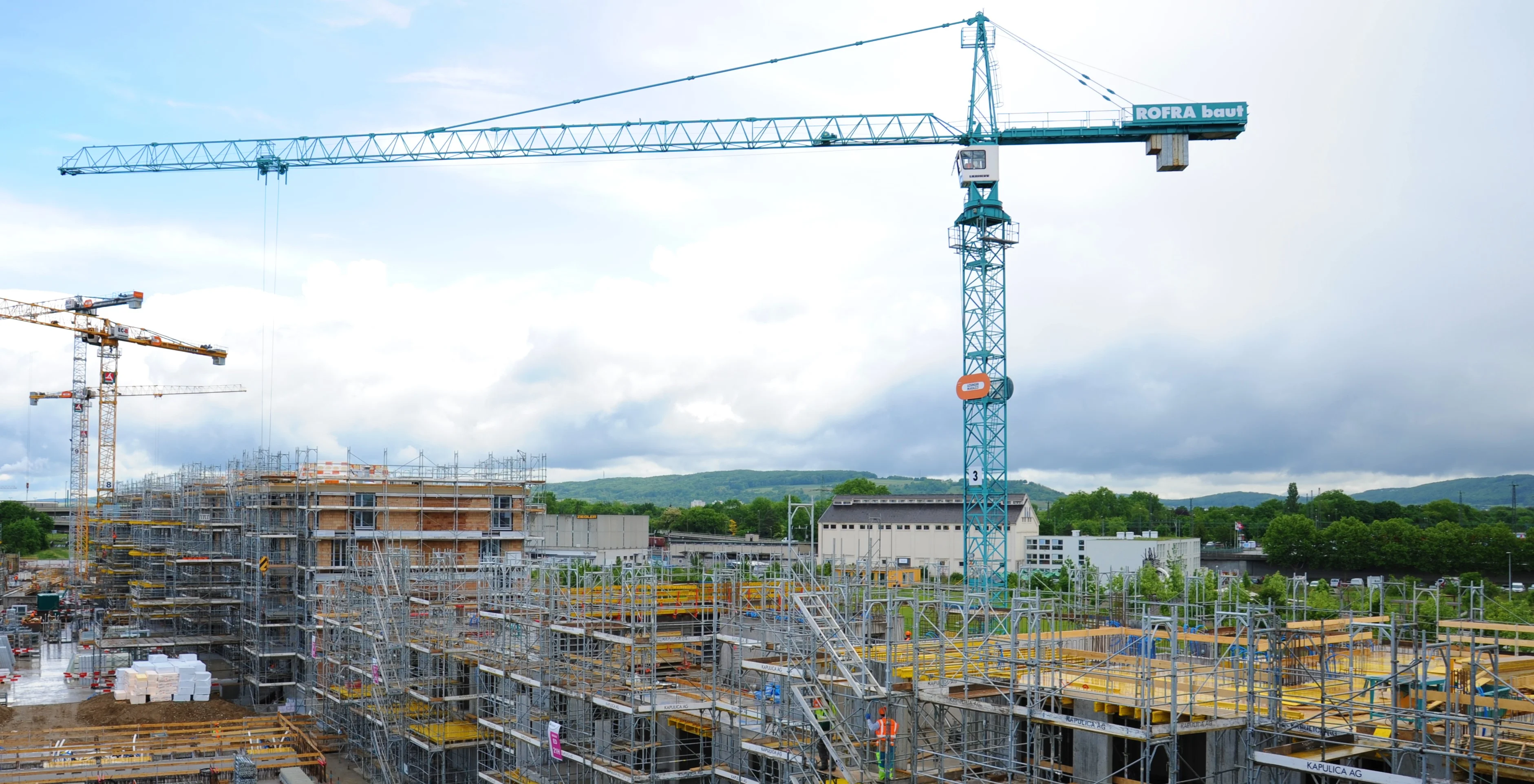 Großbaustelle mit Kränen, Gerüsten und Schalungen unter blauem Himmel