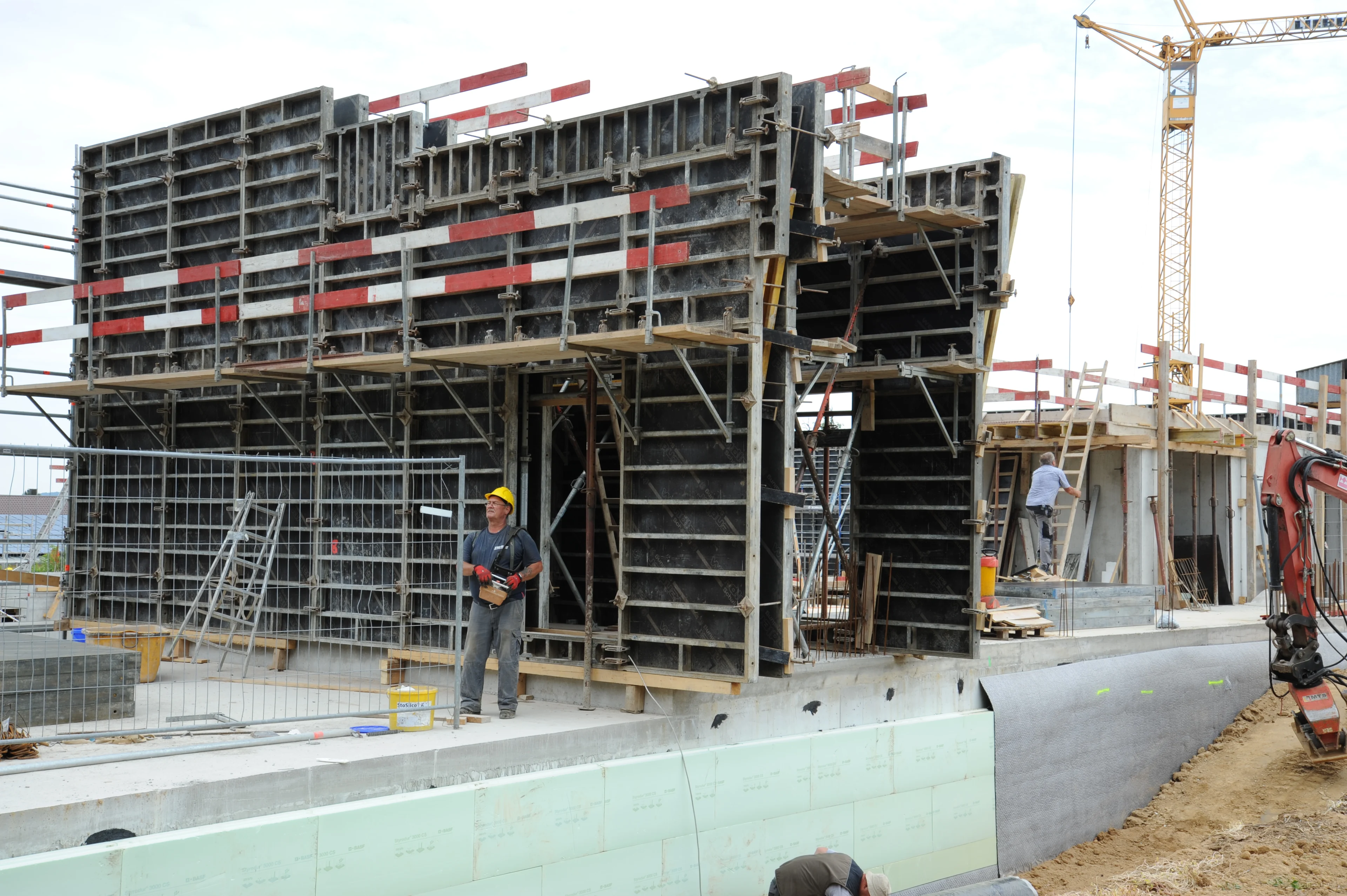 Wandschalung mit Arbeitsbühne auf einer Baustelle, Kran im Hintergrund